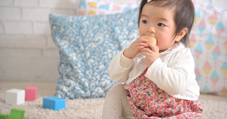 木のおもちゃをなめる赤ちゃん